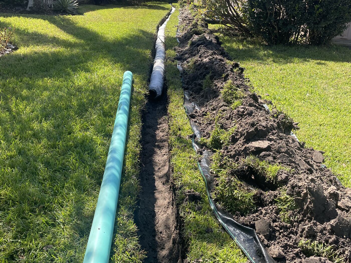 Open trench across a Carrollwood FL lawn exposing the failed original French drain pipe and filter fabric before replacement by Water Oak Irrigation