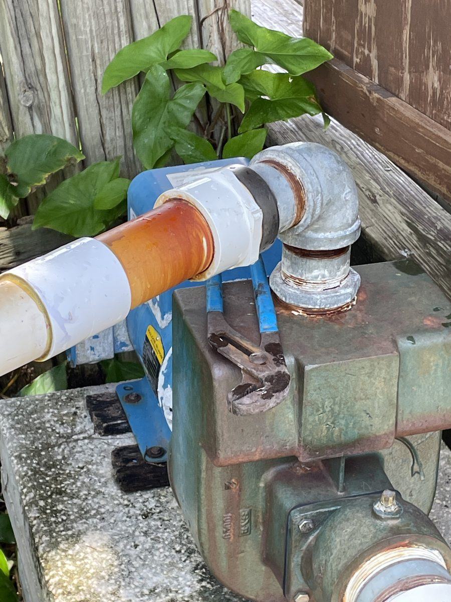 Corroded lake-drawn irrigation pump with PVC suction line and galvanized elbow awaiting repair at a Tampa, FL waterfront property
