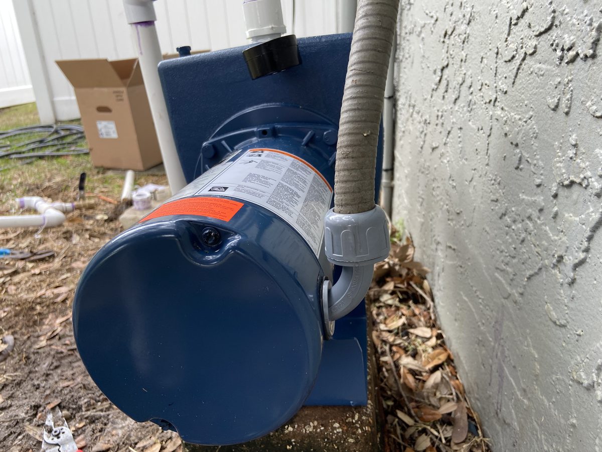 Newly installed self-priming shallow well pump with flexible suction line on a concrete pad beside a Tampa, FL home